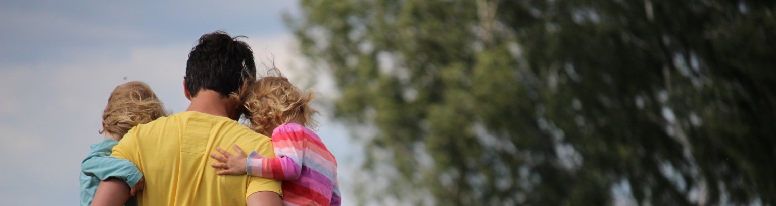 Mann trägt zwei Kinder auf dem Arm über eine Wiese