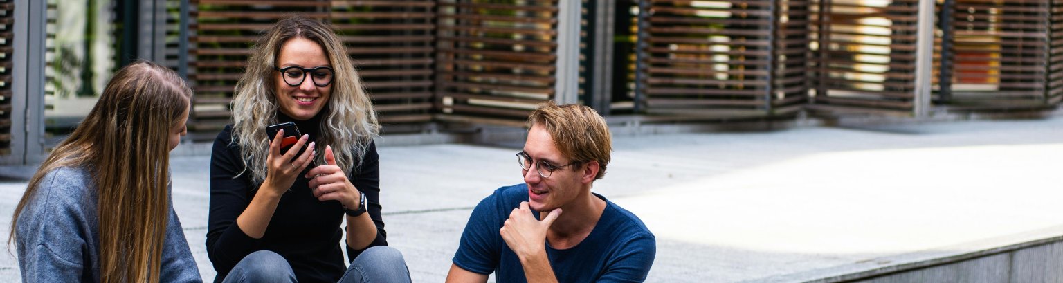 Drei junge Menschen sitzen auf Treppenstufen vor einem Gebäude.