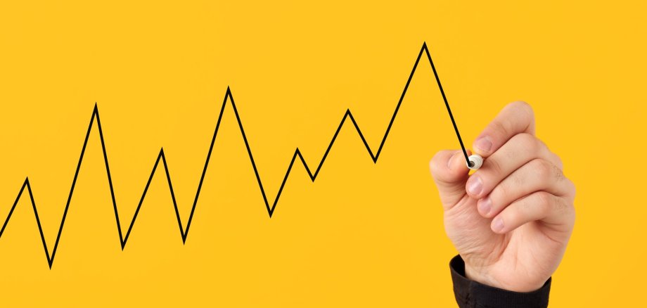 Male hand draws a fluctuating line graph on yellow background.