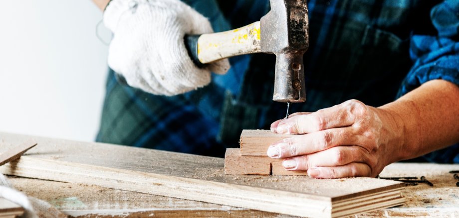 EIn Handwerker schlägt einen Nagel in zwei Bretter. 