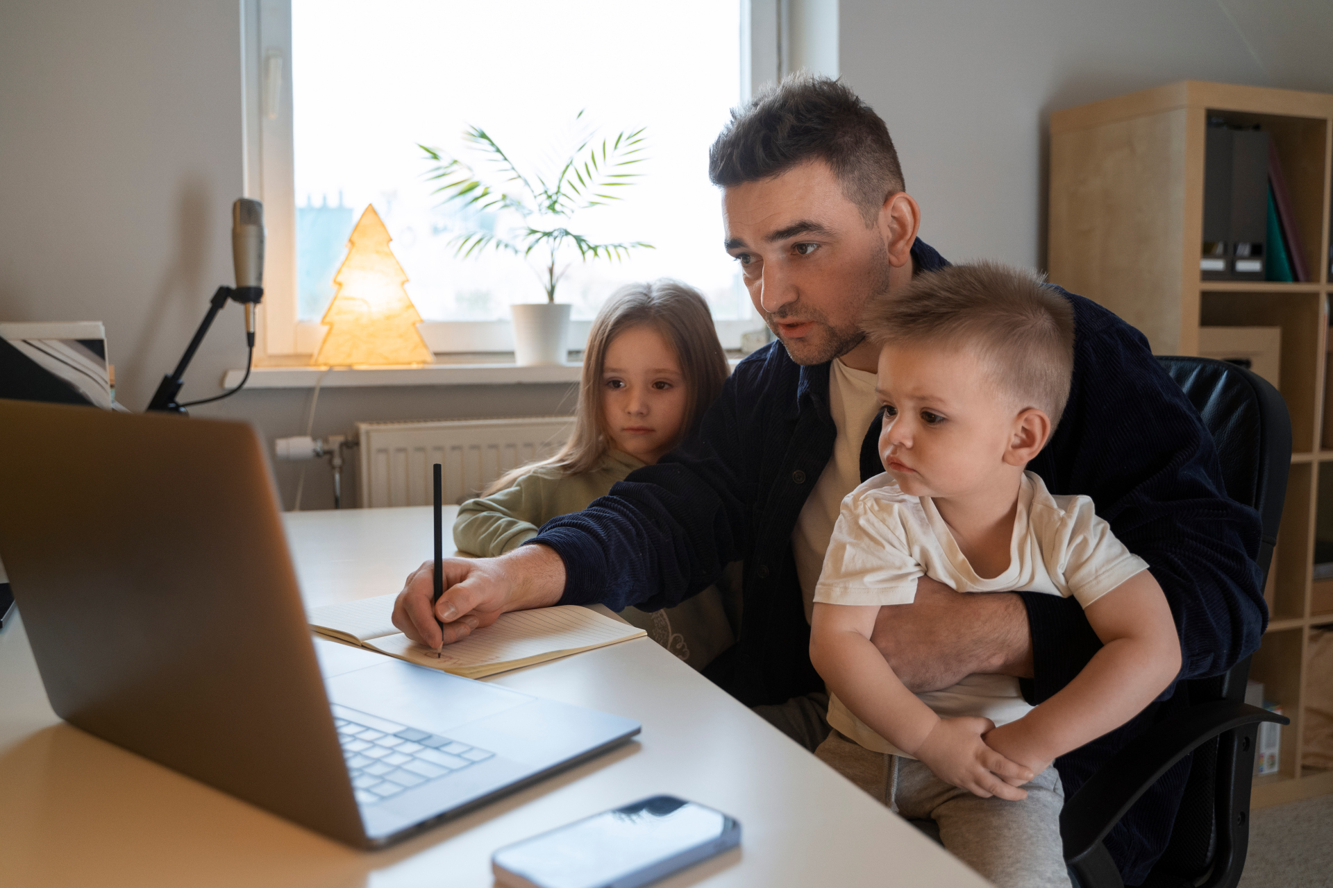 Mann sitzt mit zwei Kindern am Laptop und arbeitet