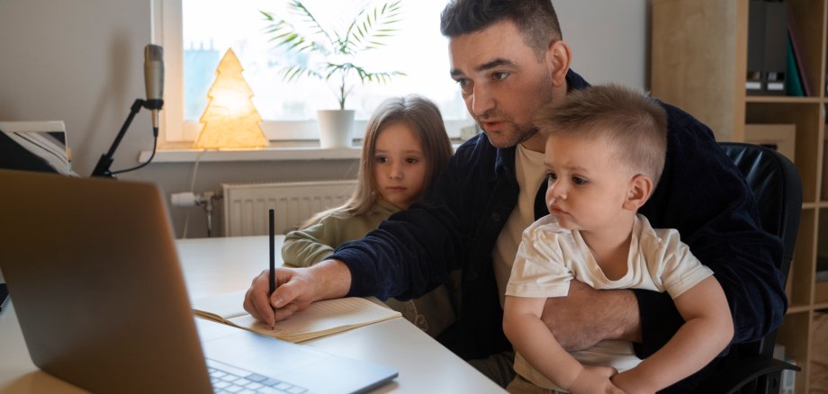 Mann sitzt mit zwei Kindern am Laptop und arbeitet