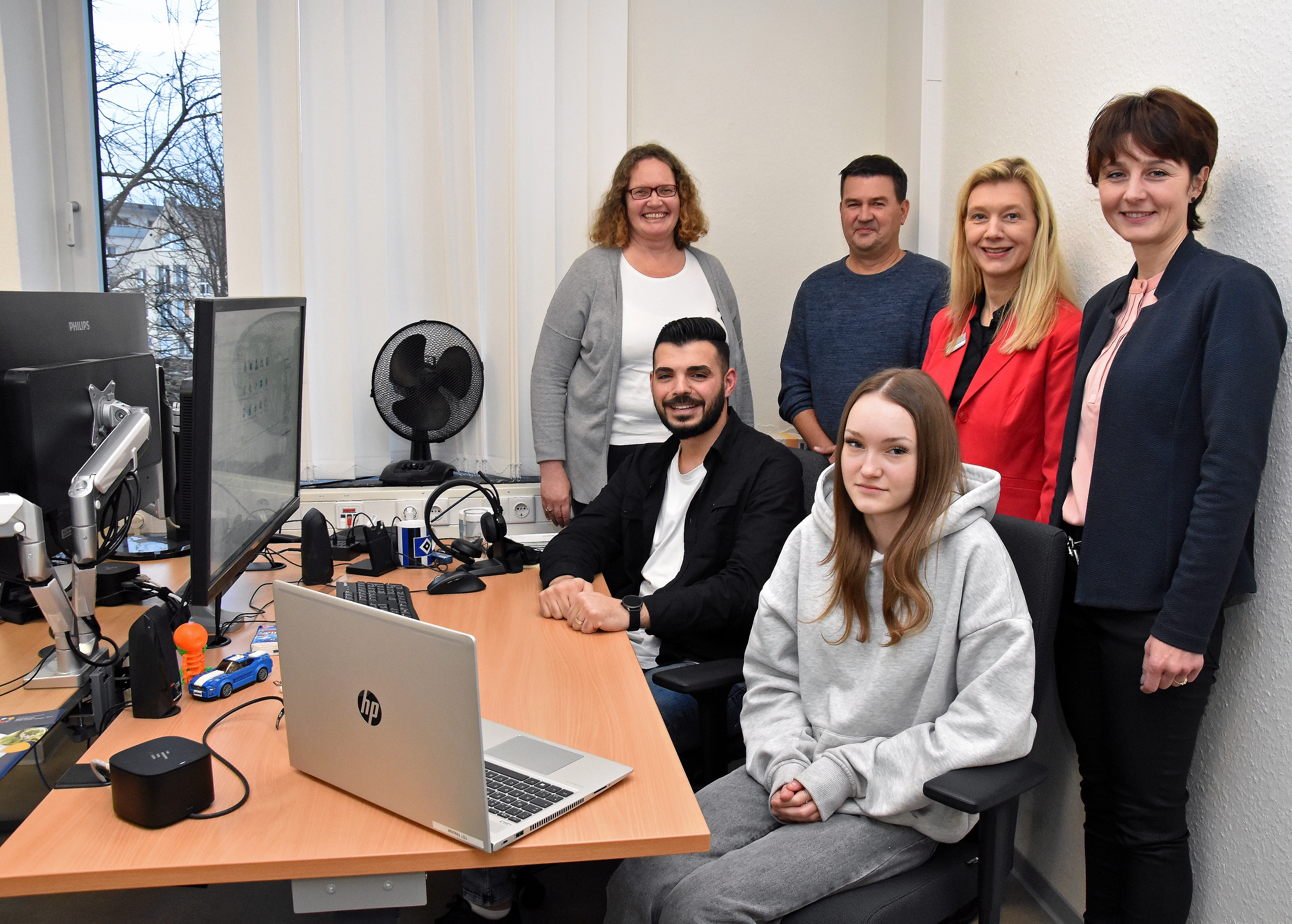 Menschen stehen an einem Schreibtisch.