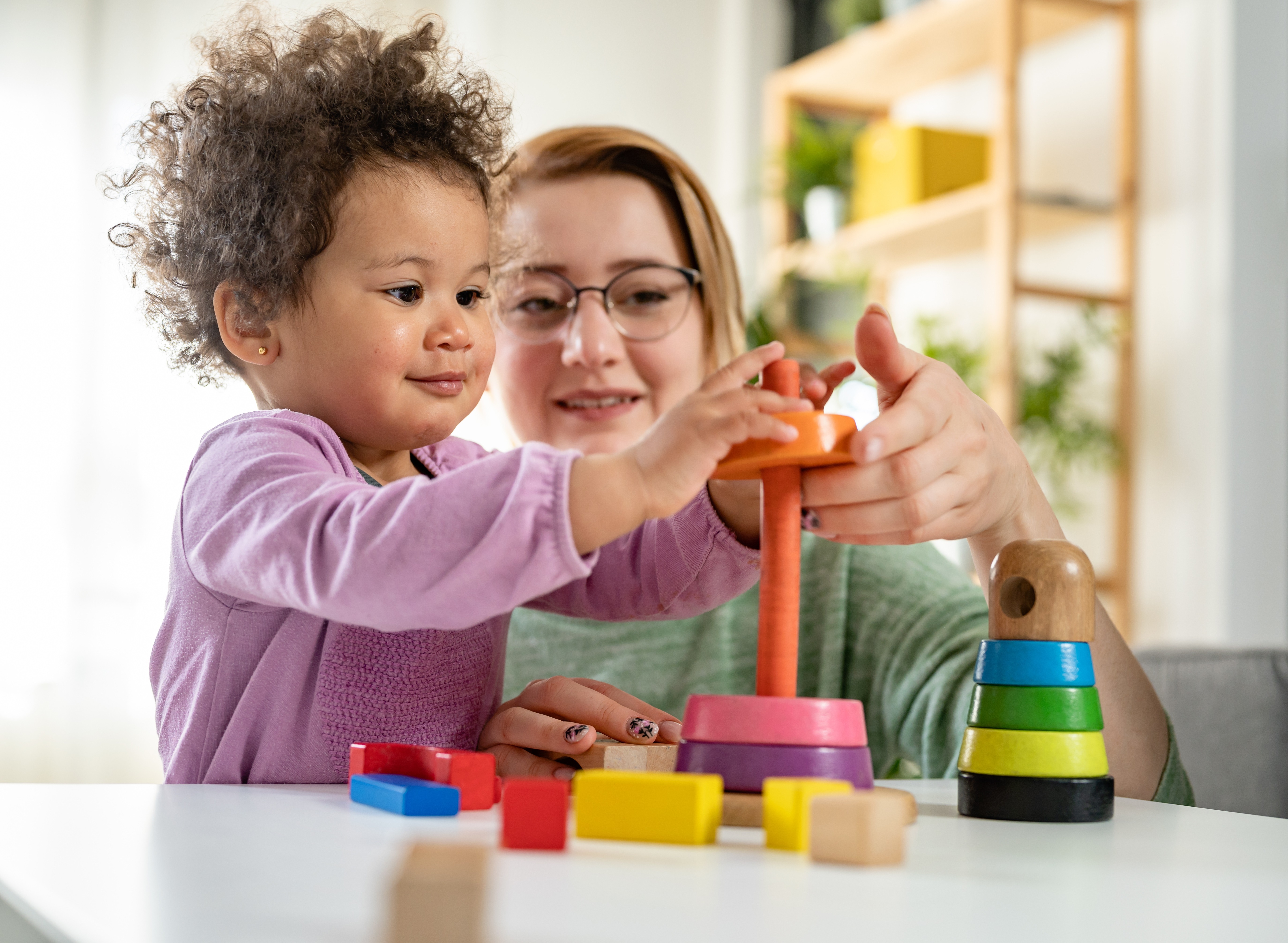 Mother looking at a child playing with an educational didactic toy. Young woman and child playing with didactic toys Mother looking at a child playing with an educational didactic toy. Young woman and child playing with didactic toys