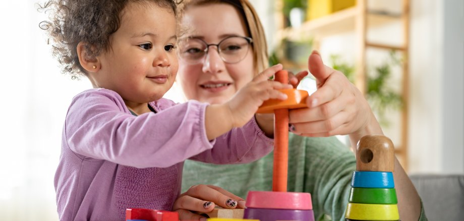 Mother looking at a child playing with an educational didactic toy. Young woman and child playing with didactic toys