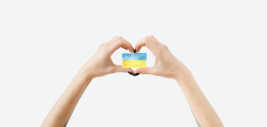Zwei Hände als Herz geformt, die eine kleine ukrainische Flagge halten.