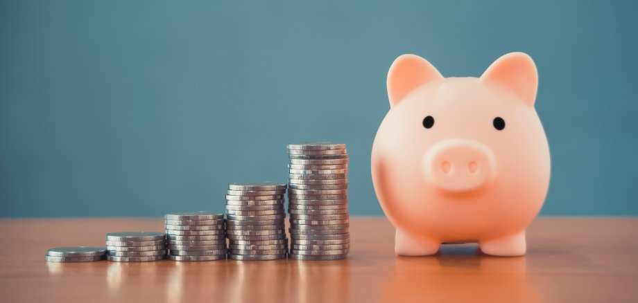 pink piggy bank and money stack tower on a wooden office desk table with blurred blue background conceptual for business finance