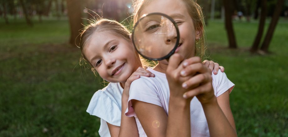 cheerful kid holding magnifier near face while standing with fri