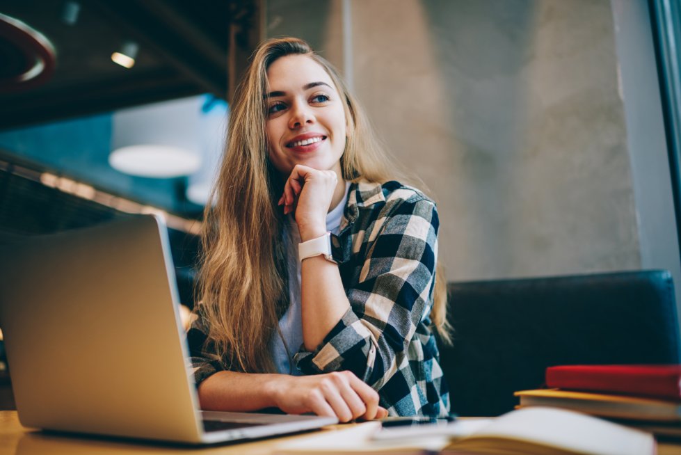 Cheerful female it developer looking at cafeteria window after work on laptop computer